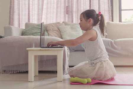 Young mixed Asian girl watching  streaming videos on laptop, workout training at home, zoom online exercises class,  social distancing conceptの写真素材
