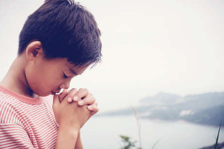 Multicultural asian boy praying with hands closed on the mountain outdoorsの写真素材