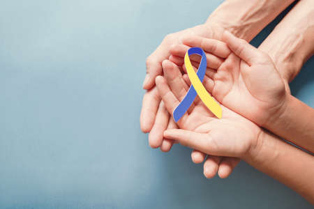 Adult and child hands holding blue and yellow ribbon shaped paper, Down syndrome awareness , World...