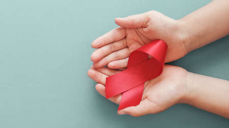 Hands holding red ribbon on red background, hiv awareness concept, world AIDS day, world...