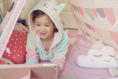 Mixed race Asian girl making video calling with tablet at home, using zoom learning online app, social distancing, isolation, homeschooling education, learning remotely conceptの写真素材