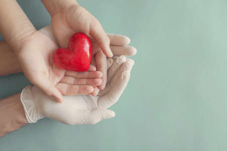 Doctor hands with medical gloves holding child hands and red heart, health insurance and donation conceptの写真素材