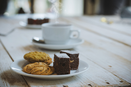 chocolate cookies and brownie in white plate on wood table with coffee cup at morning with sunrise. dessert and coffee concept.の写真素材