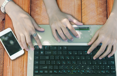 beautiful of woman hand attractive typing laptop keyboard on wooden board with smartphone.