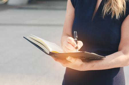 attractive business woman hand writing on notebook paper with pencil at outdoor in the city with sun light.の写真素材