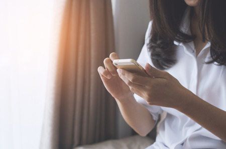 attractive woman hands using smartphone on the bed in sleeping room at morning after wake up.の写真素材