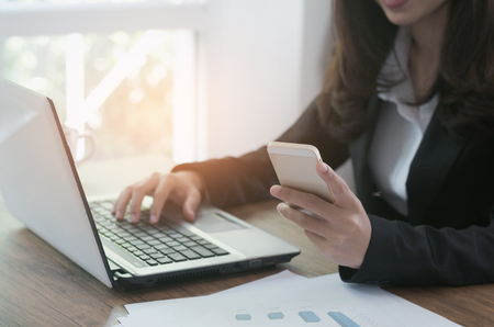 attractive woman hands using smartphone and laptop working typing keyboard on the desk in office.の写真素材