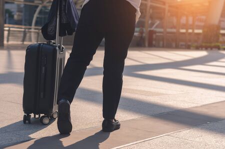 traveler girl holding and pull luggage walking on concrete floor at outdoor in the city the way go to public transport with sunlight and go to travel planning in vacation time concept.の写真素材