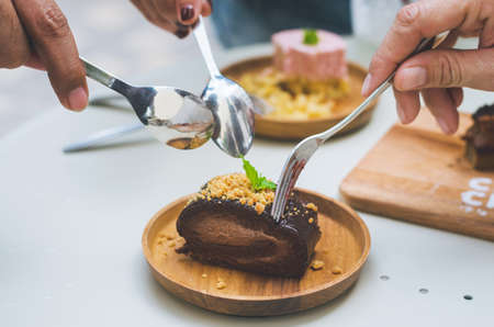 beautiful woman group eating chocolate cake in wooden plate with hands holding fork ready to put on...