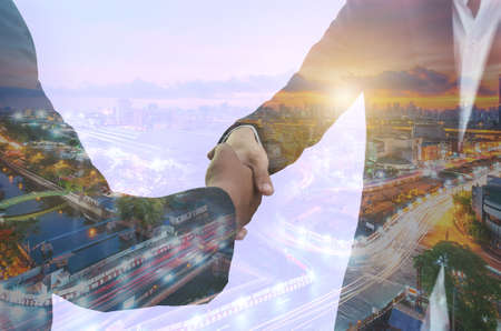 businessman shaking hand partners together agreement success business deal concept with double exposure night cityscape and buildings landscape skyline.の写真素材