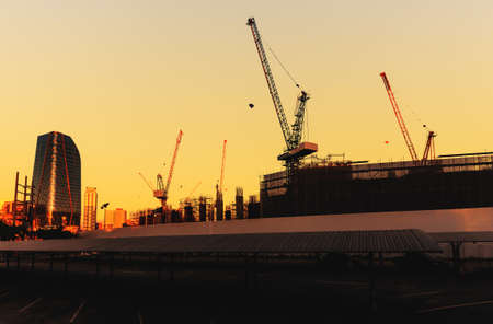 building construction site structure with crane silhouette at sunset against orange sky in city.