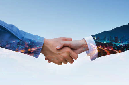 double exposure of business partner shaking hands, close up handshake businessman and businesswoman agreement deal, teamwork and partnership concept investment dealing with night cityscape background.の写真素材