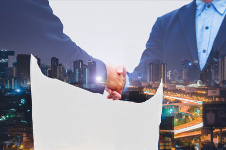 business man greeting with shaking hands partnership successful corporate dealing working together concept with double exposure of night cityscape in city metropolis landscape.の写真素材