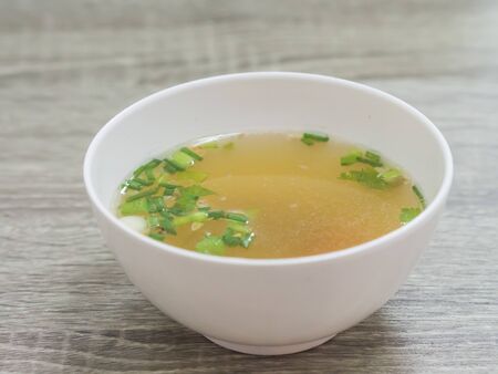 thai chicken soup  with scallion , white bowl, gray wood background