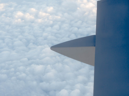 a part of air plane wing above many cloud in blue sky , air plane window view