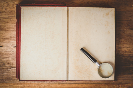 magnifying glass on open old book blank on wooden table background, top viewの写真素材