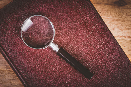 close-up magnifying glass place on old book on wooden table, vintage toneの写真素材