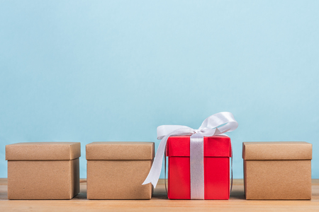 different gifts on wooden table, a red gift box tied with white ribbon is between craft boxes on...