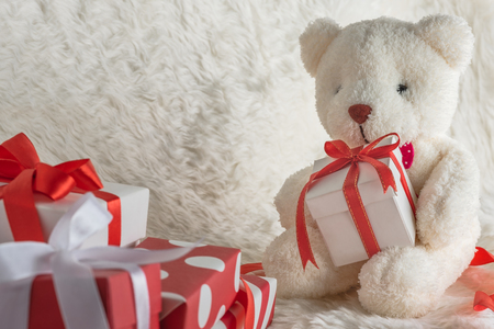 teddy bear holding a gift tied with red ribbon on wooden table, white wool backgroundの写真素材