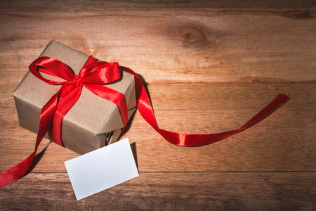 craft gift box tied with red ribbon and bow on wooden table, white blank card for textの写真素材