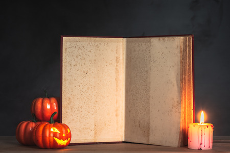 old books decorated with halloween pumpkins and horror candles, open old book to blank page for textの写真素材