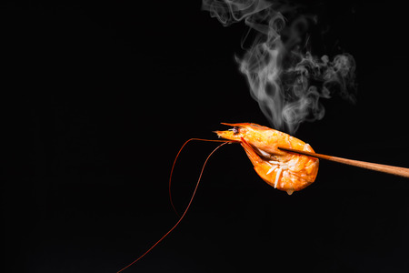 red cooked shrimp in wooden chopsticks on black background, hot food with steamの写真素材