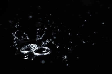 close-up of couple silver ring on black background, water drop and splash on ringの写真素材