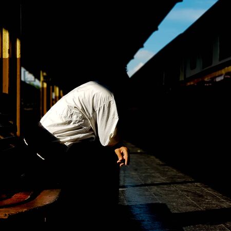 A man sits at the bench in Hua lamphong train station in Bangkok, Thailand with a cigarette in his hand.の写真素材