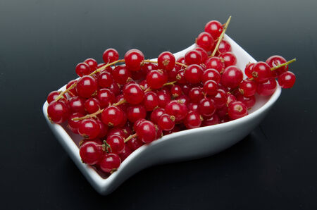 Redcurrants in a small dish on a black backgroundの写真素材