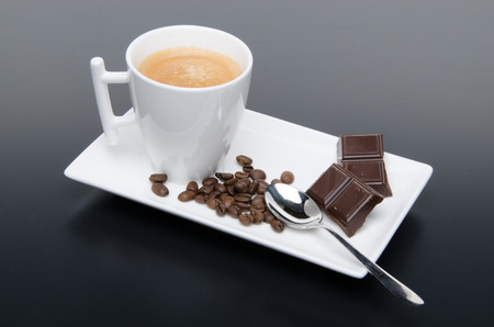 A cup of coffee with chocolate and coffee beans on a black backgroundの写真素材