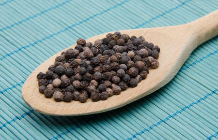 Pepper in a wooden spoon on a blue straw matの写真素材