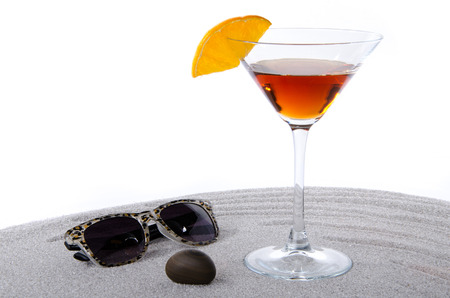 Cocktail glass with sunglasses and a pebble on the sand on white backgroundの写真素材