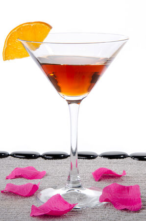 Cocktail glass with sunglasses, a flower petals and  black pebbles on grey sandの写真素材