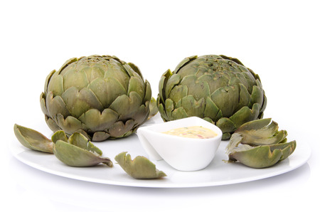 Cooked artichoke with a vinaigrette sauce on a plate, isolated on whiteの写真素材