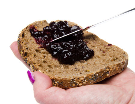Woman's hand putting blackberry jam on a toast, isolated on whiteの写真素材