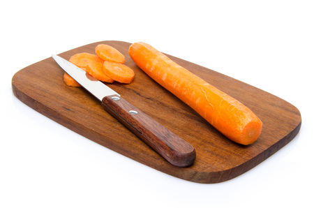 Carrot slices on a wood cutting board with a knife, isolated on whiteの写真素材