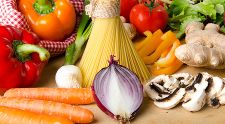 Composition of uncooked spaghetti and different types of vegetables on a wooden boardの写真素材