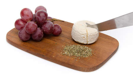 Goat cheese, grapes and provencal herbs on a wooden cutting board, isolated on whiteの写真素材