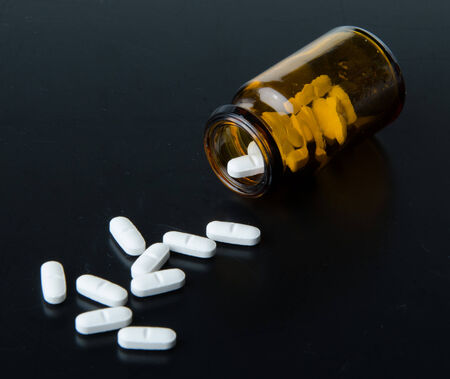 Pills spilling out of pill bottle on a black backgroundの写真素材