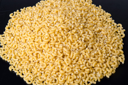 Mound of uncooked pasta elbow macaroni on a black backgroundの写真素材