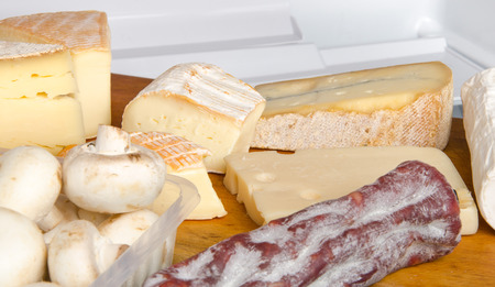 Different cheeses, mushrooms and a sausage inside a refrigeratorの写真素材