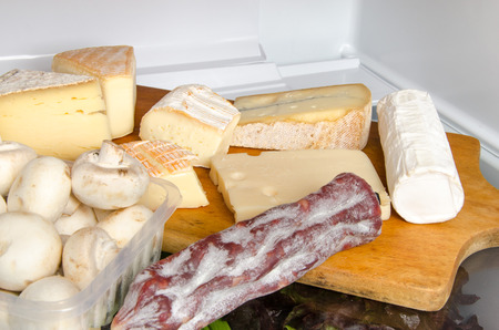 Different cheeses, mushrooms and a sausage inside a refrigeratorの写真素材