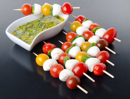 Cherry tomatoes and mozzarella on skewers and a vinaigrette sauce with basil, on a black backgroundの写真素材