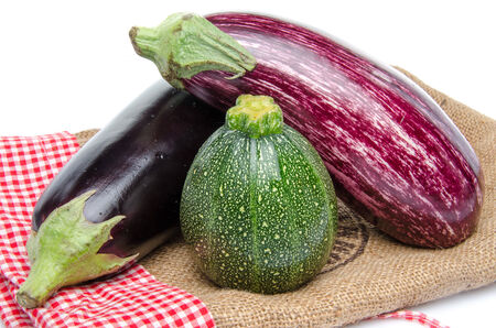 Eggplants and a zucchini on a burlap bag, isolated on whiteの写真素材