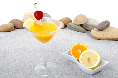 Composition with a orange cocktail on a background of sand and pebble stonesの写真素材