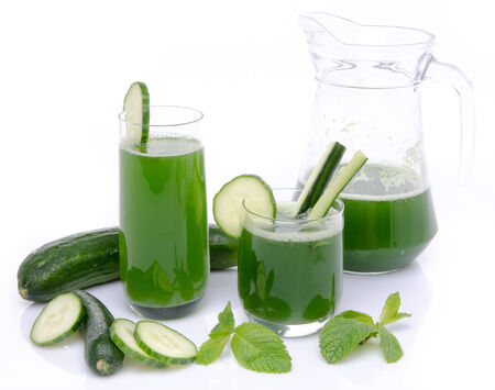 Composition with two glasses and a jug of cucumber juice, fresh cucumbers and mint, isolated on whiteの写真素材