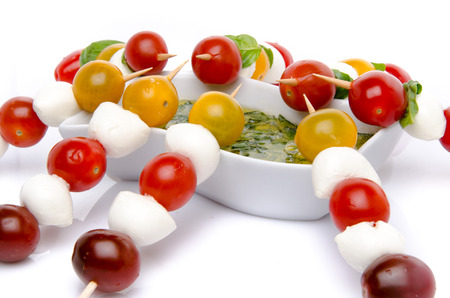 Cherry tomatoes and mozzarella on skewers and a vinaigrette sauce with basil, isolated on whiteの写真素材