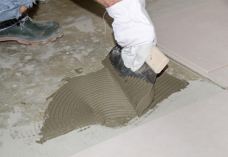 Laying tiles, tiler spreading tile adhesive on the floorの写真素材