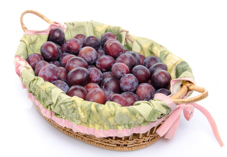 Fresh ripe blue plums in a basket, isolated on whiteの写真素材