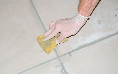 Laying floor tiles, tiler smoothing tile joints with a sponge